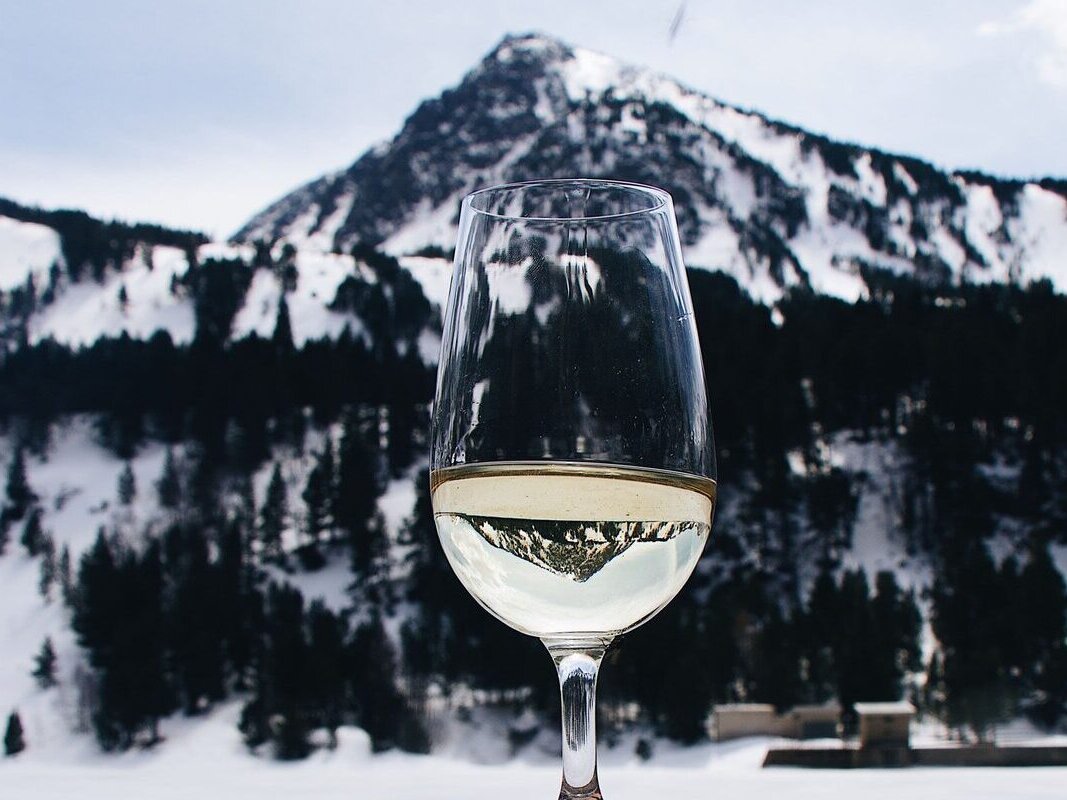 A glass of chilled white wine held up in front of a snowy Alpine peak (an illustration of a dry white, not a Savoie label)
