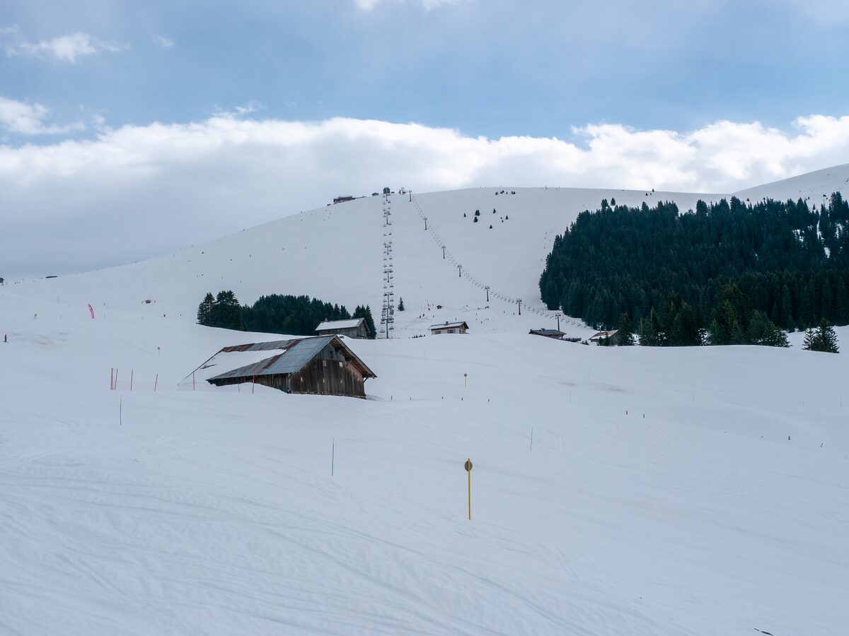 A chairlift line climbing a wide snowy slope at Mont Joux above Saint-Gervais, with a wooden barn half buried in snow (the snowpark is not in the frame)