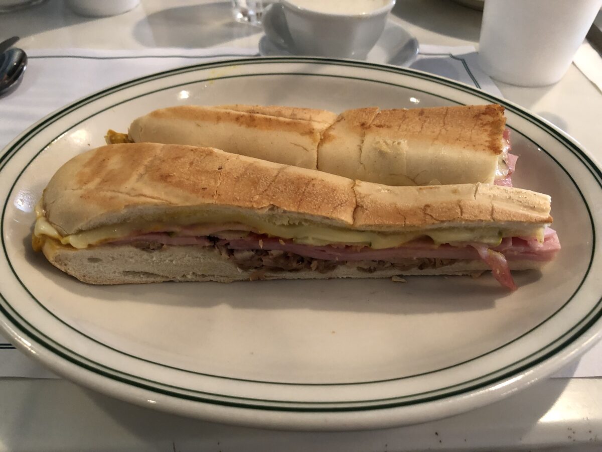 A pressed Cuban sandwich cut in half on a plate, with ham, roast pork and melted Swiss cheese between slices of Cuban bread