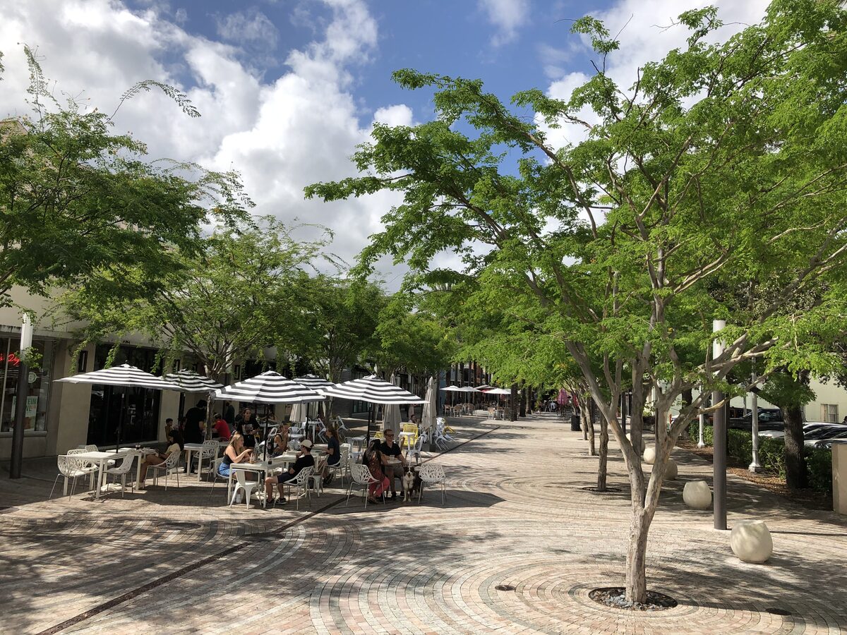 Giralda Plaza in Coral Gables, a pedestrian street lined with trees and cafe tables under umbrellas