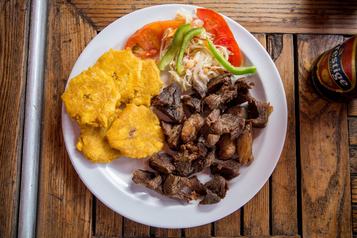 A plate of Haitian griot, fried pork chunks, with fried plantain, pikliz slaw and tomato