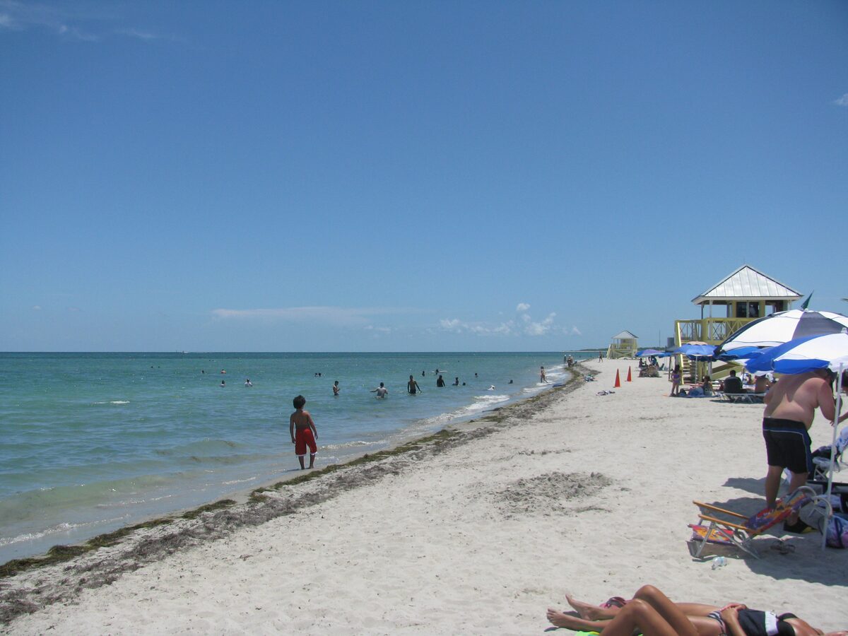 A wide white-sand beach on Key Biscayne at Crandon Park, with calm turquoise water, swimmers and a lifeguard tower under a clear sky
