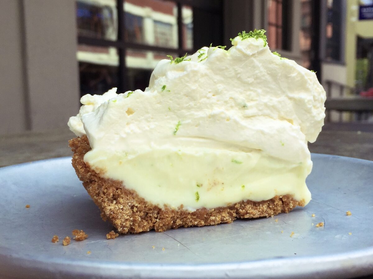 A slice of key lime pie with a graham cracker crust, pale green filling and a high swirl of whipped cream