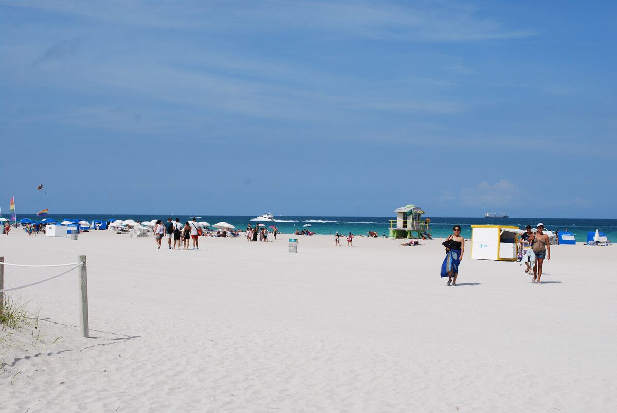 The wide white-sand beach of South Beach under a blue sky, with a lifeguard tower and strollers near the water