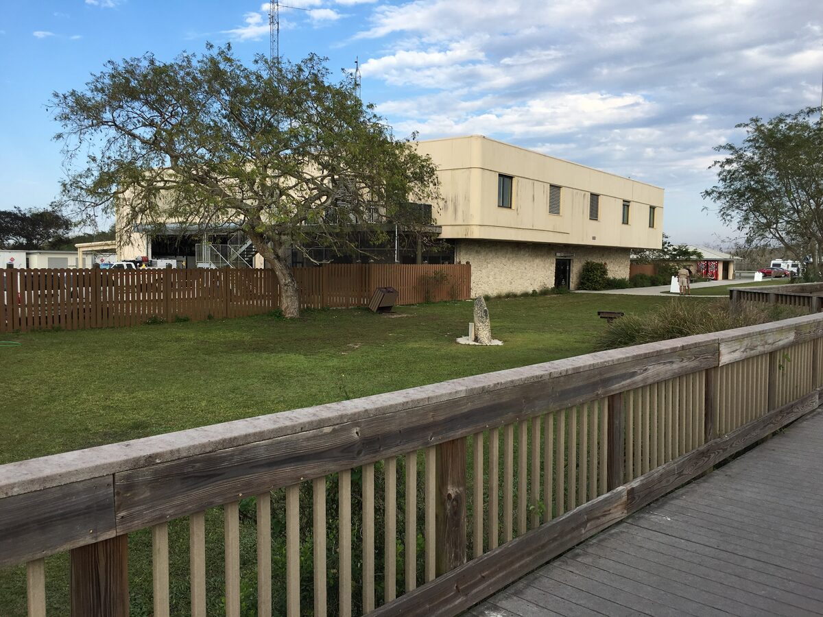 The Oasis Visitor Center in Big Cypress, a low building behind a lawn and a wooden boardwalk rail