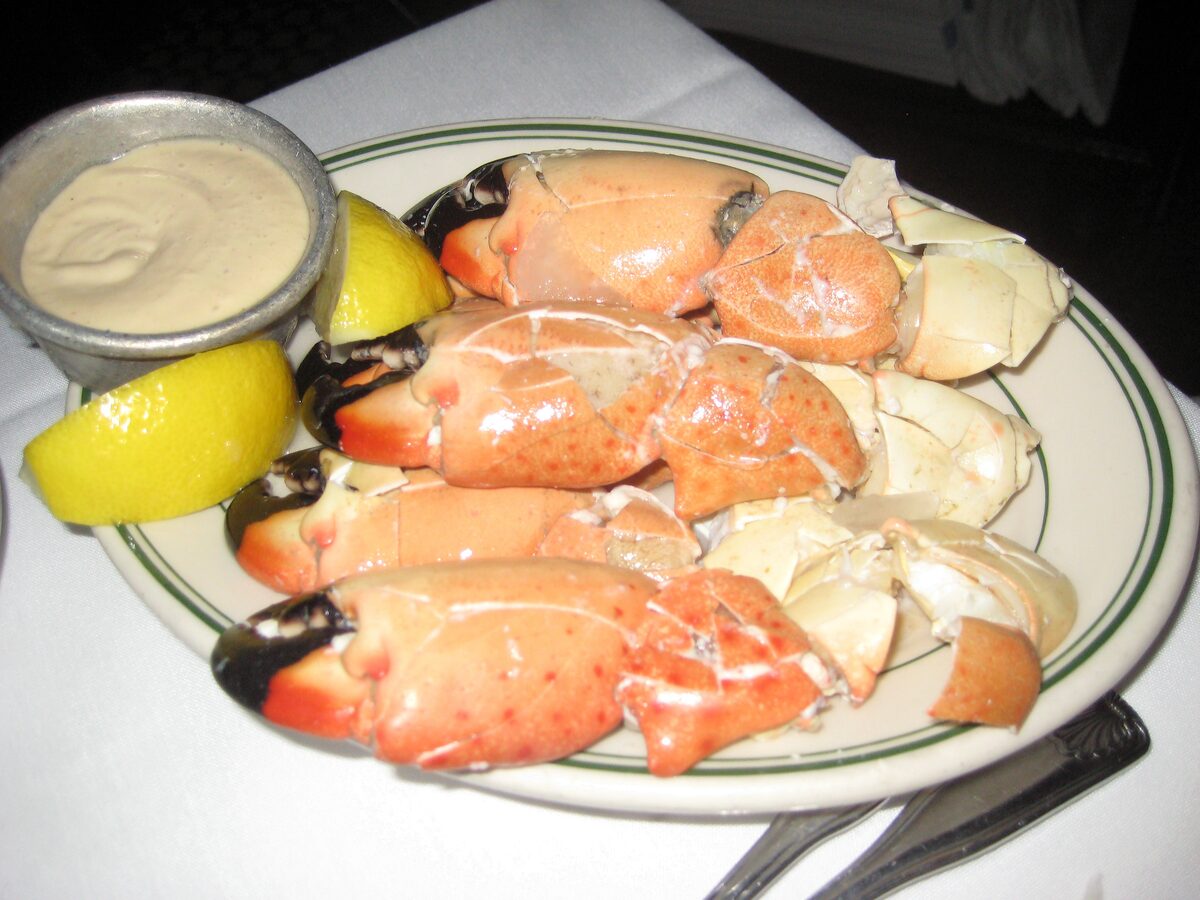 A plate of cracked stone crab claws with lemon wedges and a dish of mustard sauce at Joe's