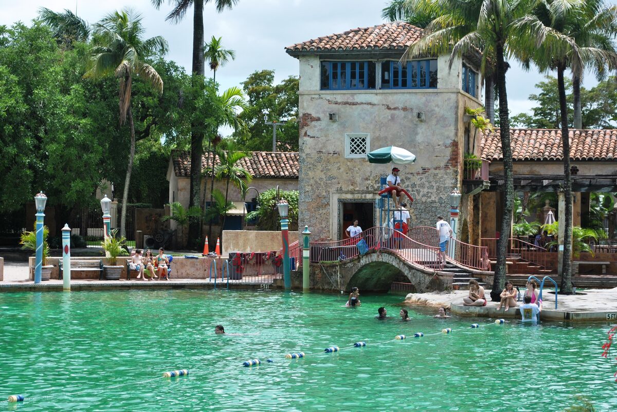 Turquoise water of the Venetian Pool in Coral Gables, with a small stone bridge, a tower and palms behind