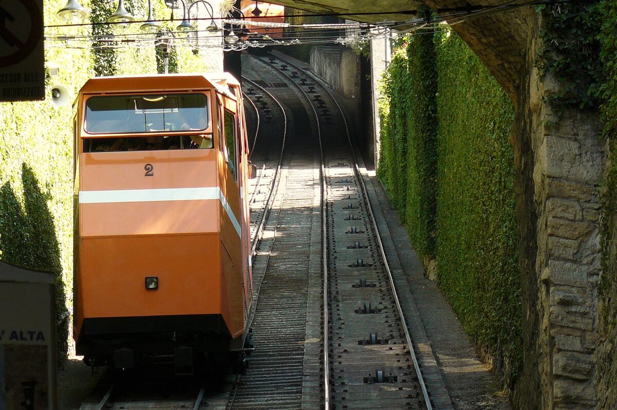 An orange funicular car on its track between ivy-covered walls