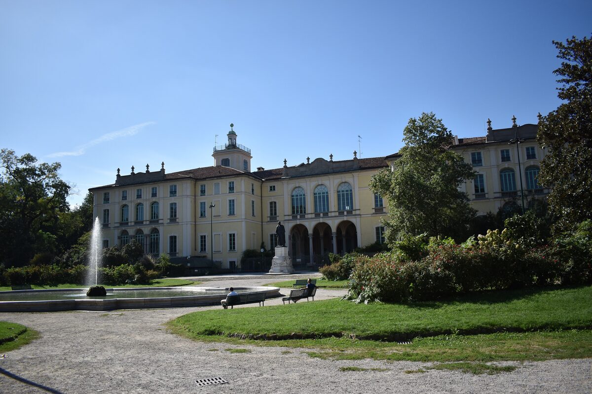 A fountain and lawn in the Giardini Pubblici, with a palazzo behind