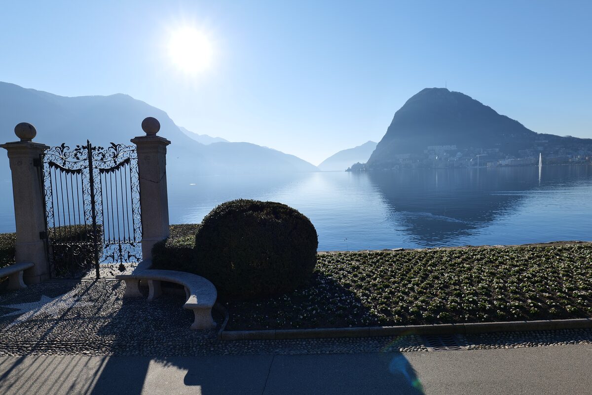 A wrought-iron gate framing Lake Lugano and its mountain
