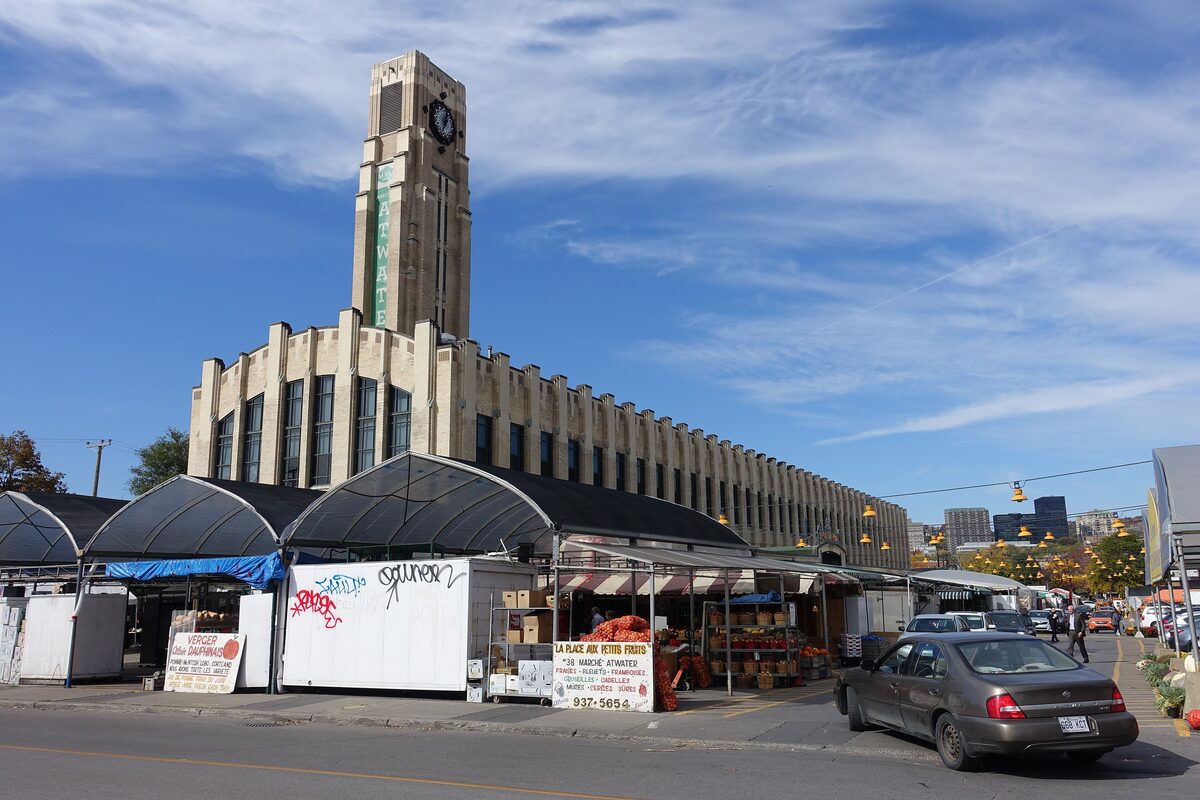 The Art Deco clock tower and long cream-colored hall of Atwater Market, with fruit and flower stalls under awnings in front