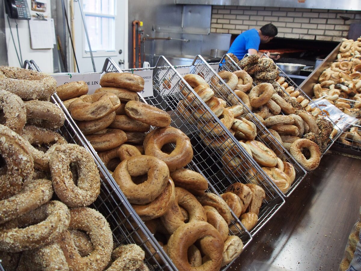 Wire racks piled with sesame and poppy-seed bagels beside the wood-fired oven of a Montreal bagel bakery