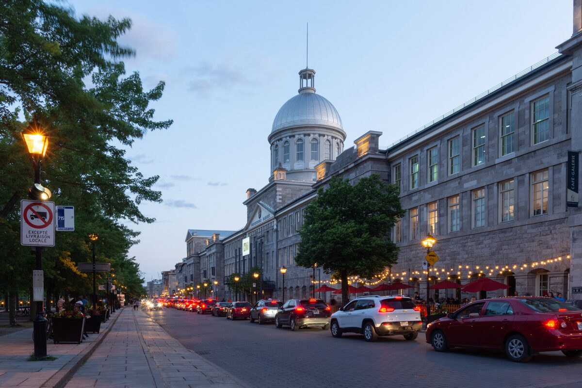 The domed Bonsecours Market on Rue Saint-Paul at dusk, with string lights over the sidewalk and cars parked along the street