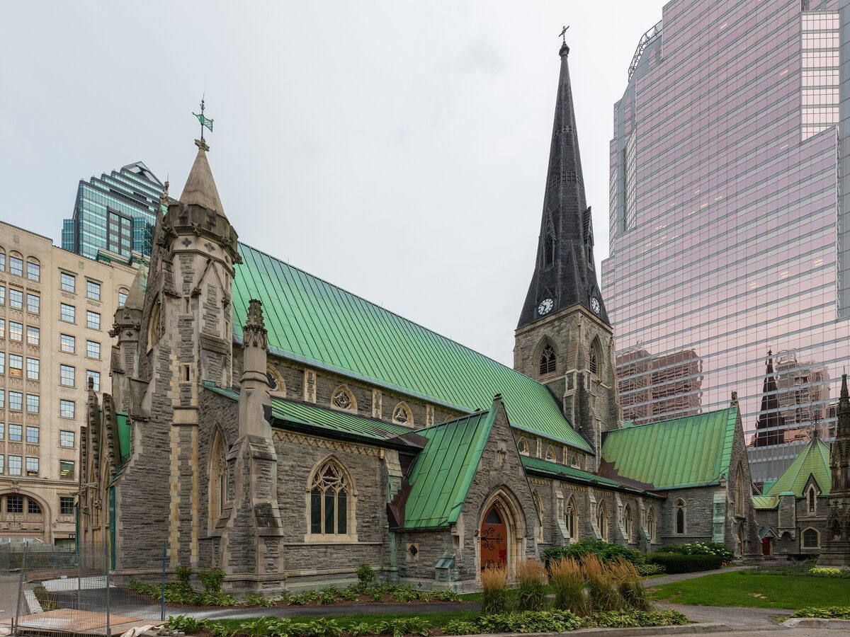 Christ Church Cathedral, a grey stone Gothic church with a green copper roof and a tall spire, squeezed between glass office towers