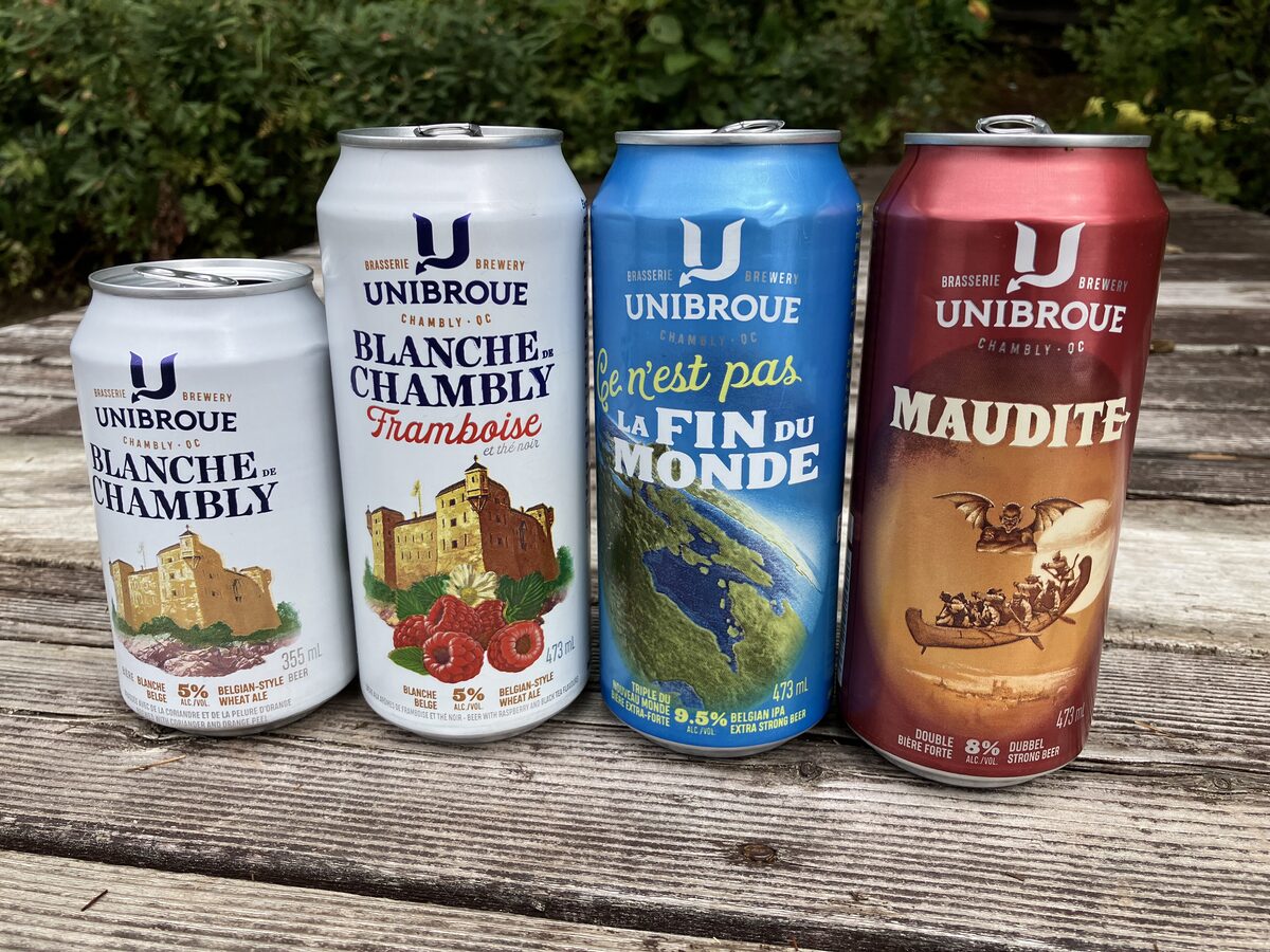 Four Unibroue beer cans on a wooden table: Blanche de Chambly, La Fin du Monde and Maudite