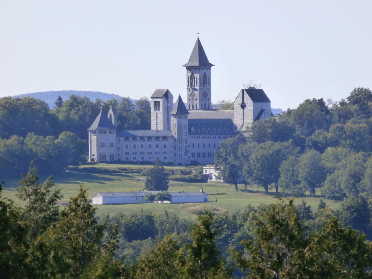 Saint-Benoît-du-Lac Abbey, a pale stone monastery with a square bell tower, on a wooded hill above green fields