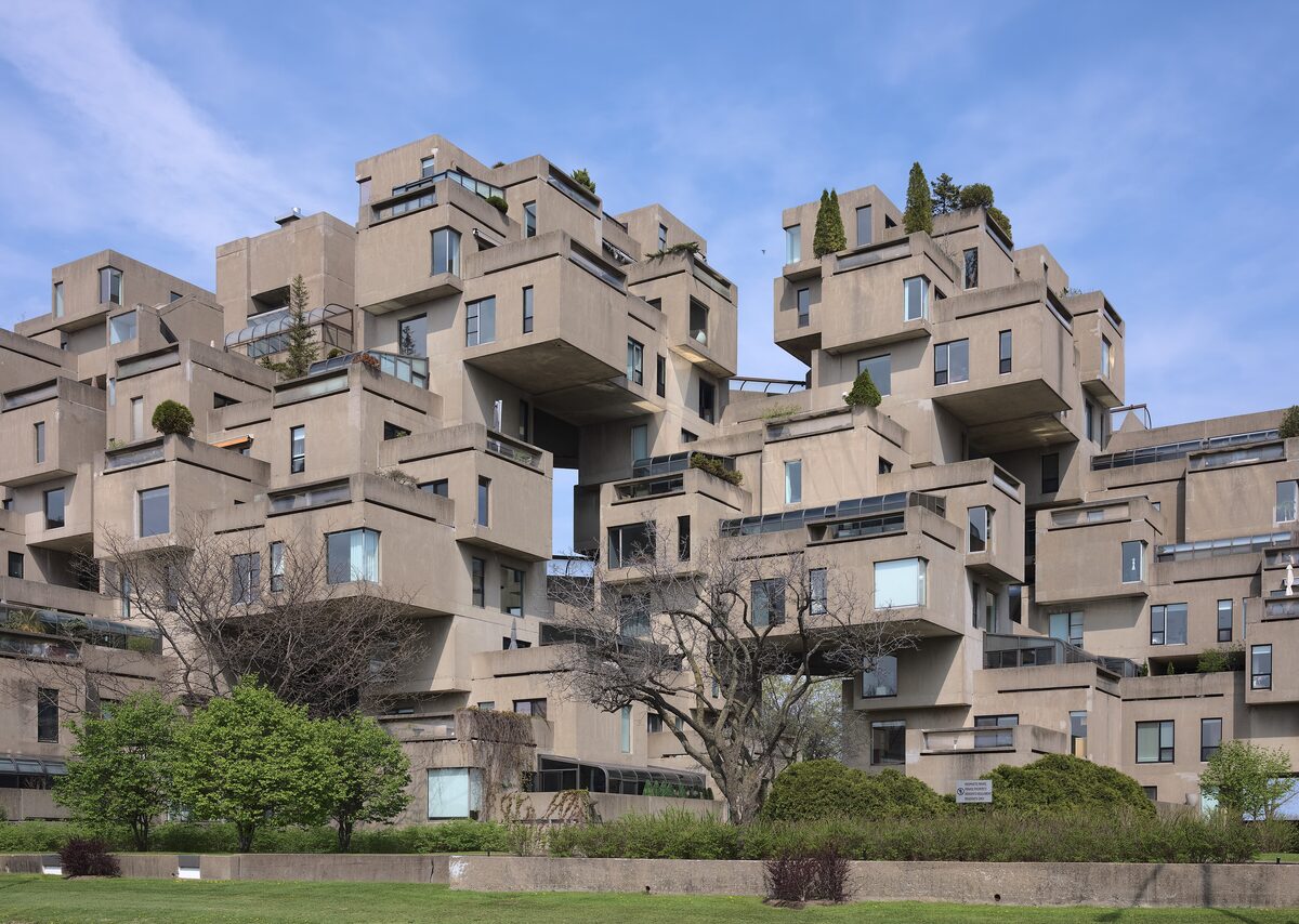 Habitat 67, the stacked concrete boxes of Moshe Safdie's housing complex, seen from the grass below under a blue sky