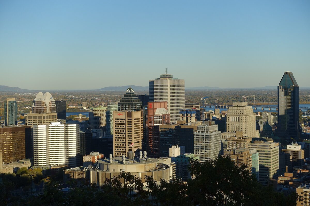 Downtown Montreal's office towers seen from the Kondiaronk Belvedere on Mount Royal, with the St. Lawrence and distant hills behind