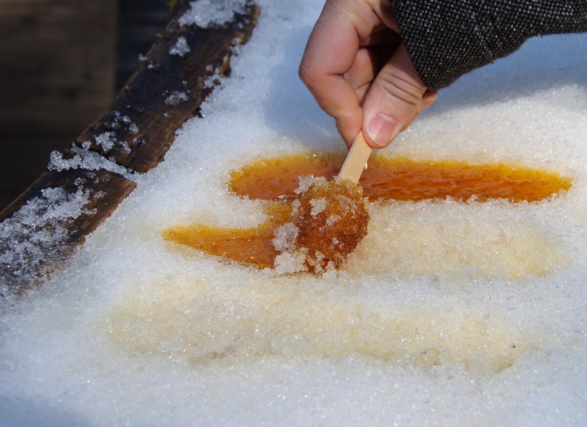 Hot maple syrup poured on packed snow and rolled onto a wooden stick, a hand lifting the amber taffy