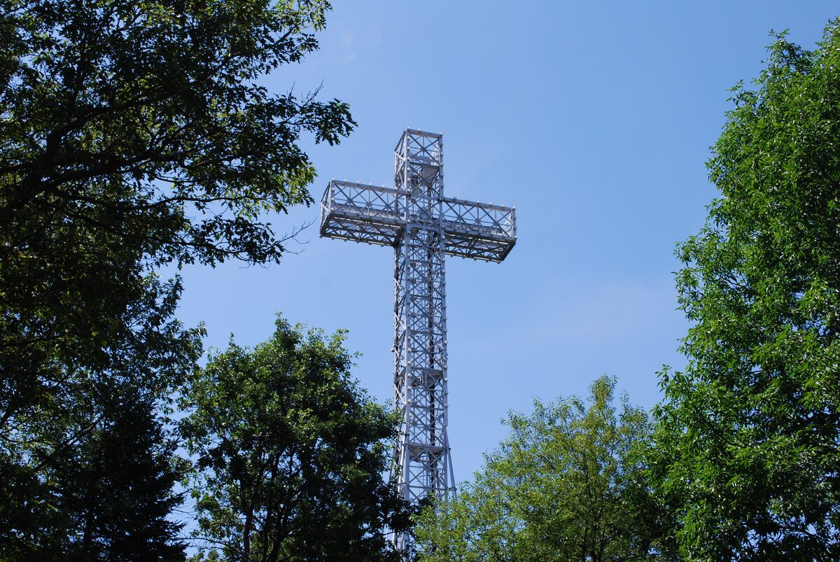 The steel lattice Mount Royal Cross seen from below through green trees under a clear sky