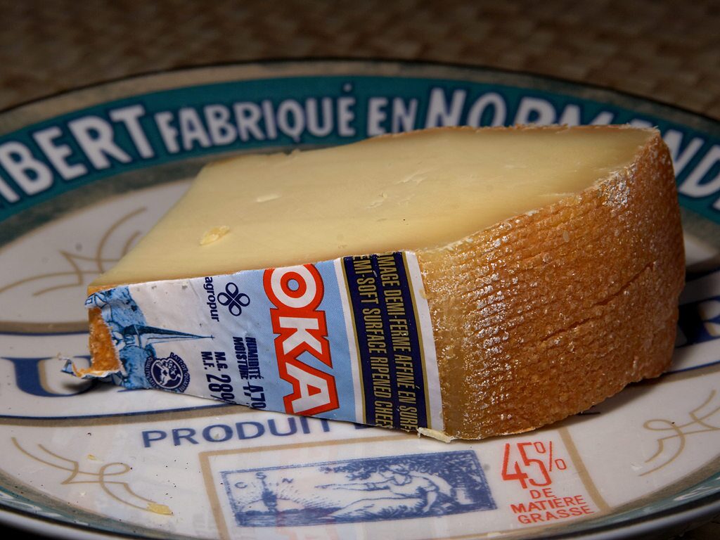 A wedge of Oka, the semi-soft Quebec cheese with its orange rind and blue-and-white label, on a plate