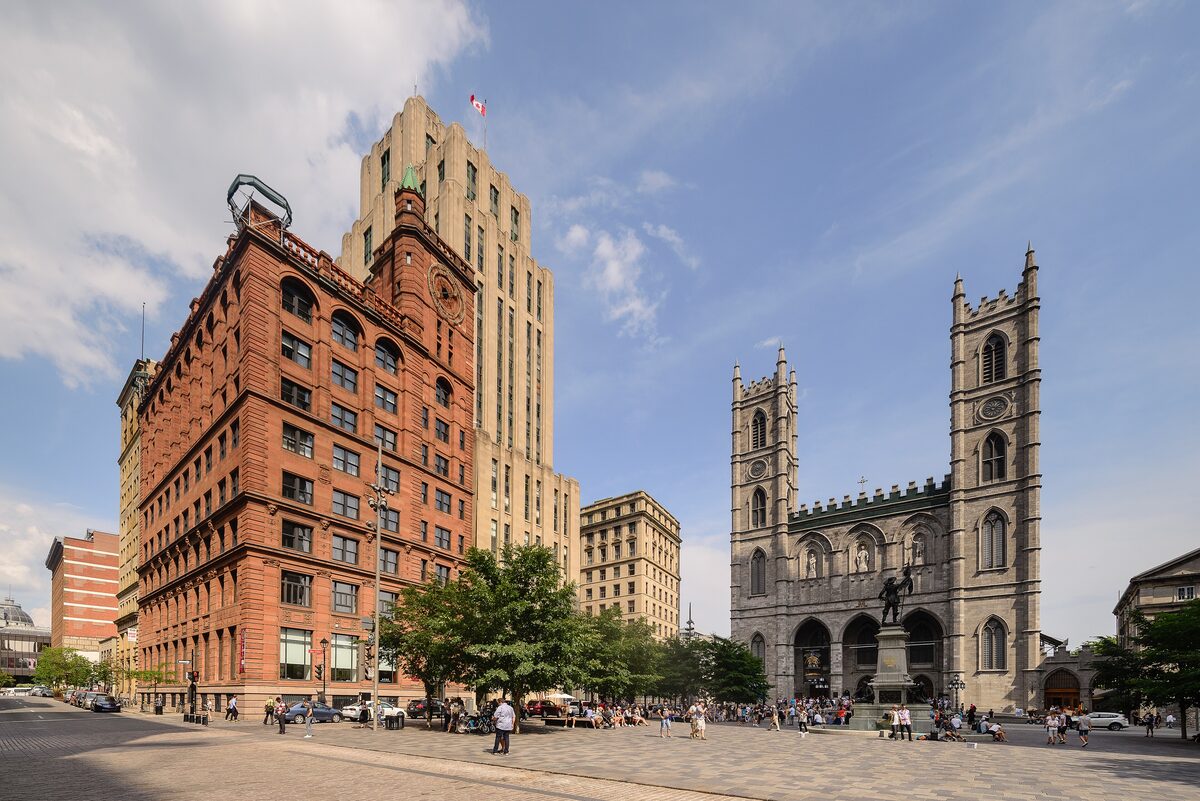 Place d'Armes with the twin towers of Notre-Dame Basilica on the right and red-brick office buildings on the left, under a blue sky