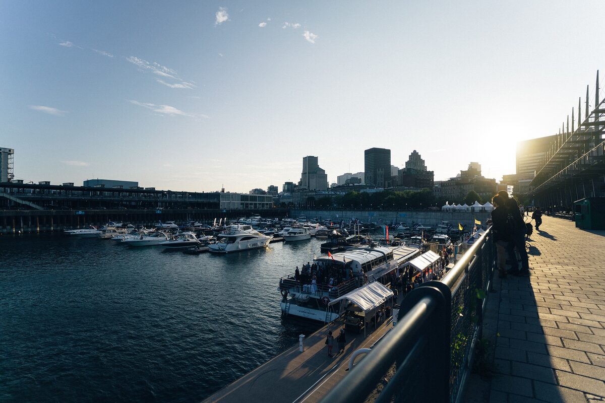 Boats moored in the Old Port basin in low sun, with the downtown skyline behind and the paved waterfront promenade on the right