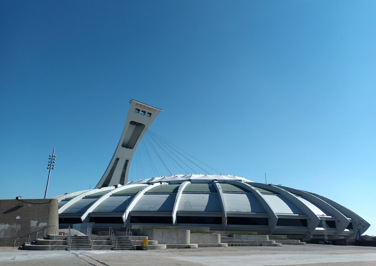 The Olympic Stadium's ribbed white roof with the leaning Montreal Tower rising behind it against a clear blue sky