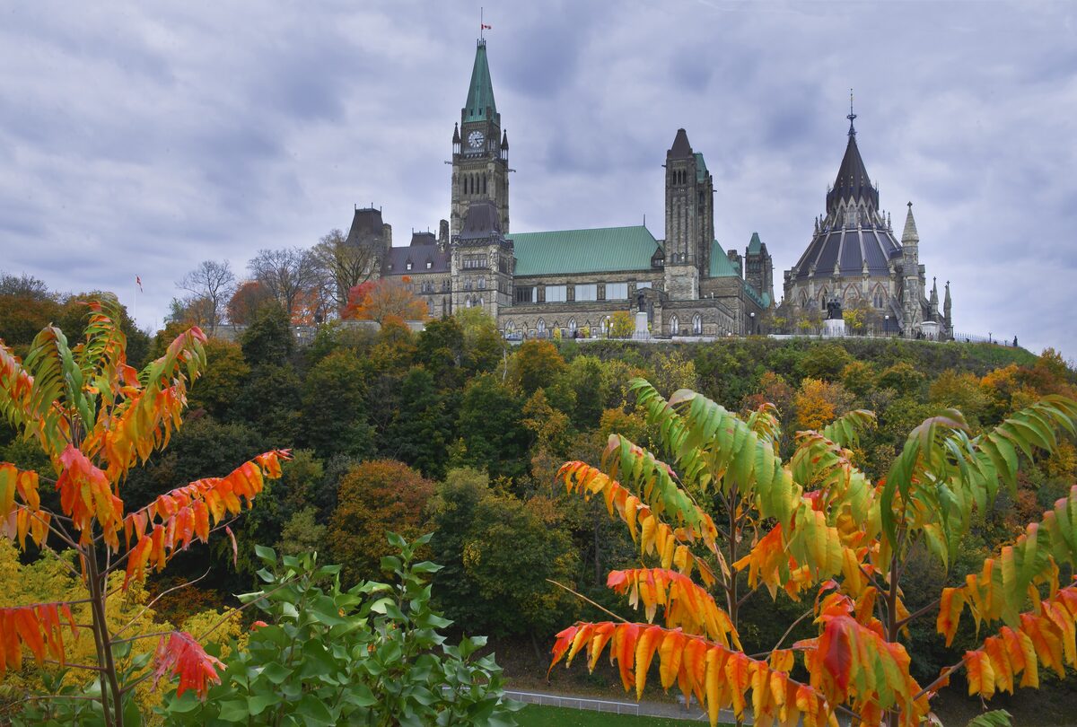 Parliament Hill in Ottawa, the green-roofed Centre Block and its clock tower above autumn trees on the river bluff
