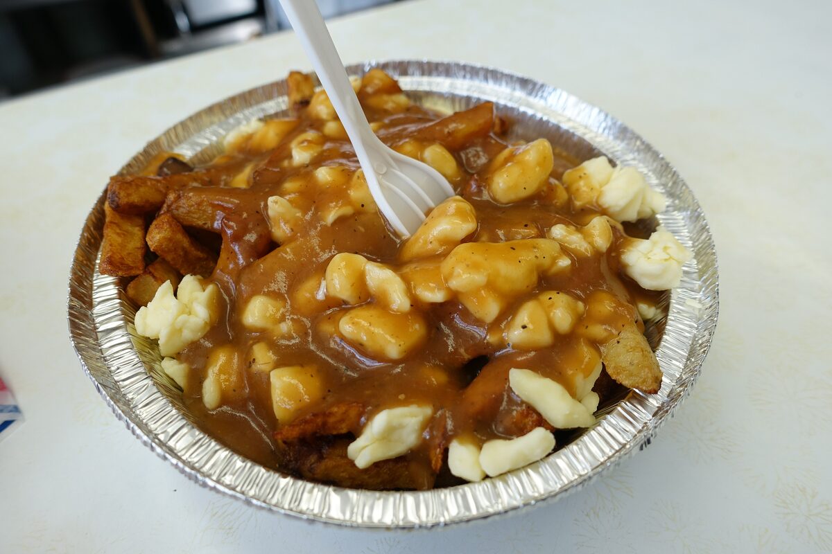 Poutine in a foil tray with a plastic fork: fries covered in brown gravy and white cheese curds