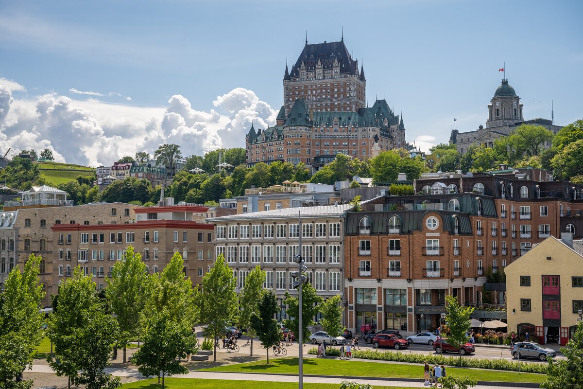 The Château Frontenac rising above the lower town of Quebec City on a sunny summer day, with trees and a lawn in the foreground