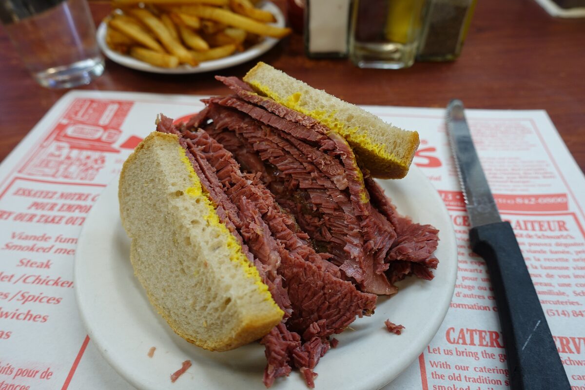 A smoked meat sandwich on rye with mustard on a plate at Schwartz's, thick pink brisket slices spilling from the bread