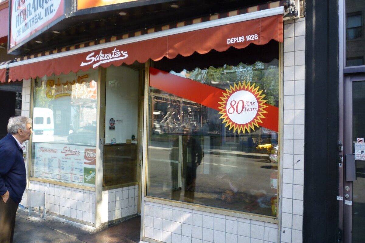 The storefront of Schwartz's Deli on Boulevard Saint-Laurent, with its red scalloped awning marked Depuis 1928 and an 80 years sticker on the window