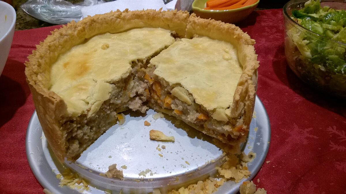 A slice cut from a meat pie, showing the spiced ground-meat filling inside a golden crust on a red tablecloth