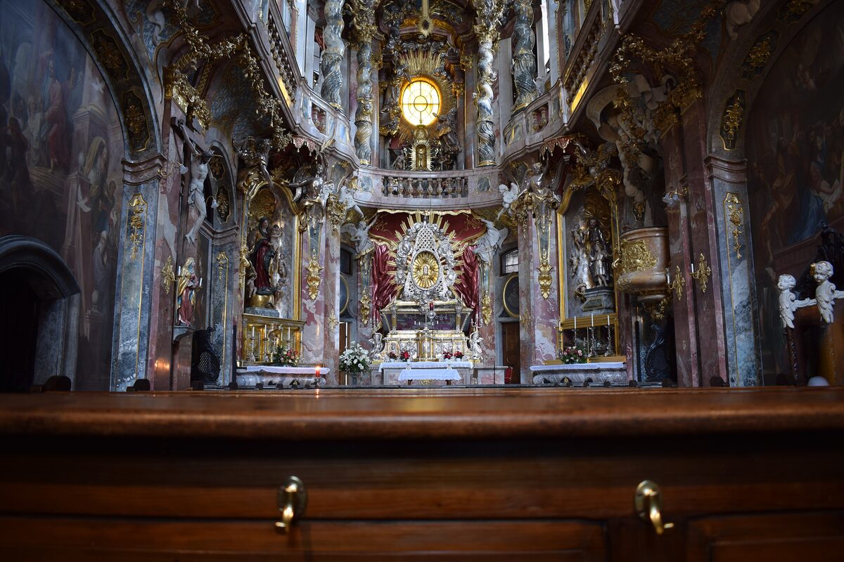 The gilded high altar of the Asamkirche glowing above a wooden pew, with stucco and frescoes on both sides