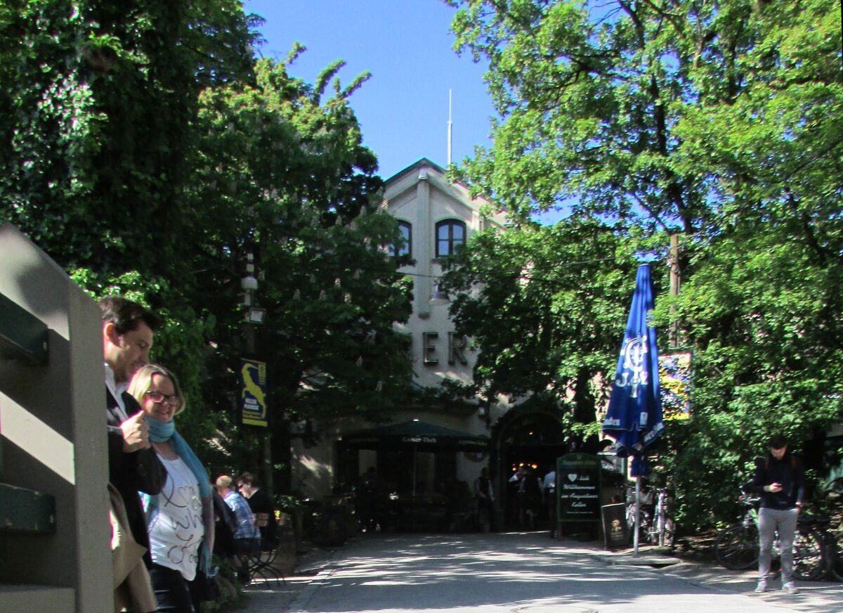 A shady gravel path in the Augustiner-Keller beer garden under tall trees, with the Keller building behind