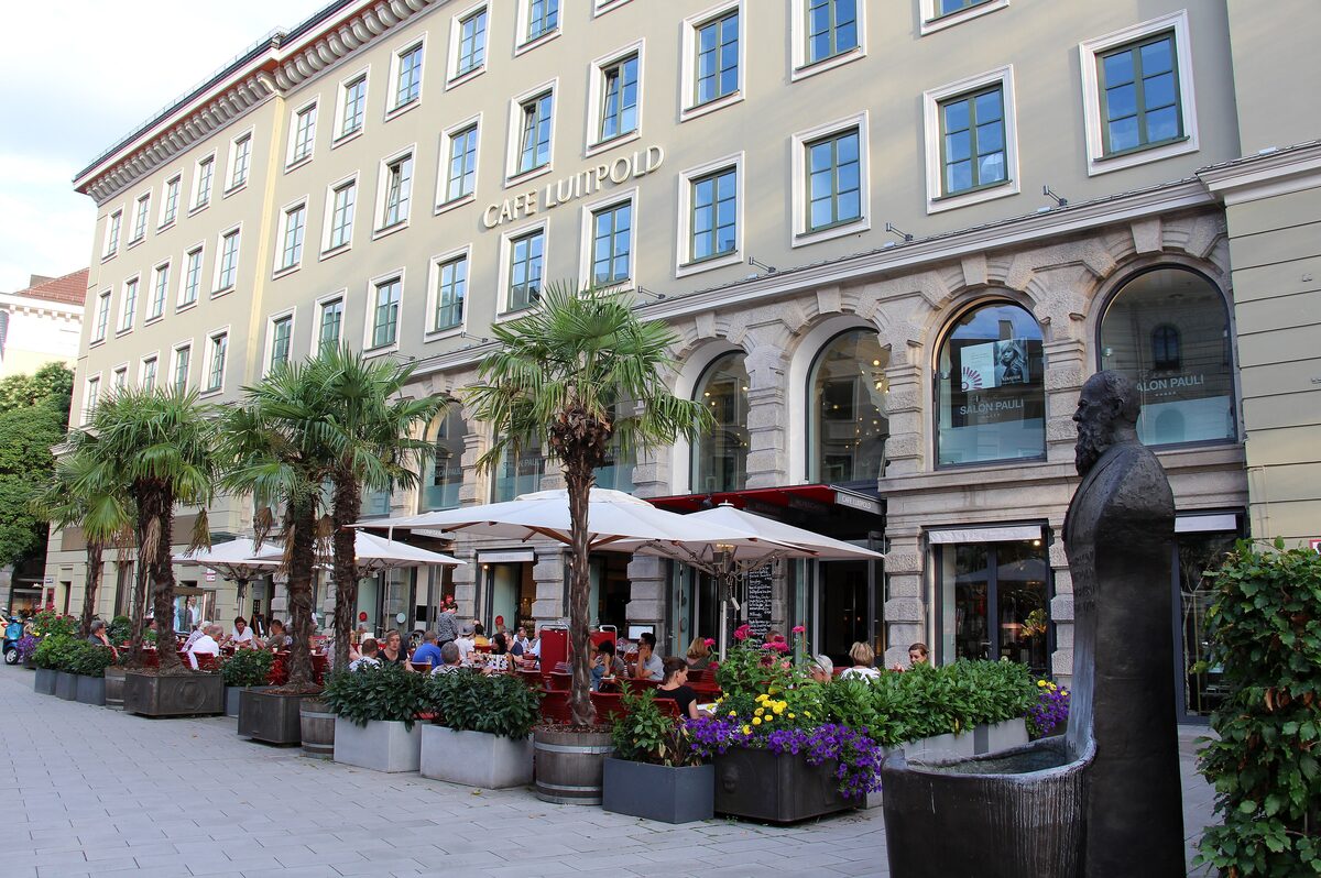The corner of Café Luitpold with palm trees and umbrellas over the terrace tables