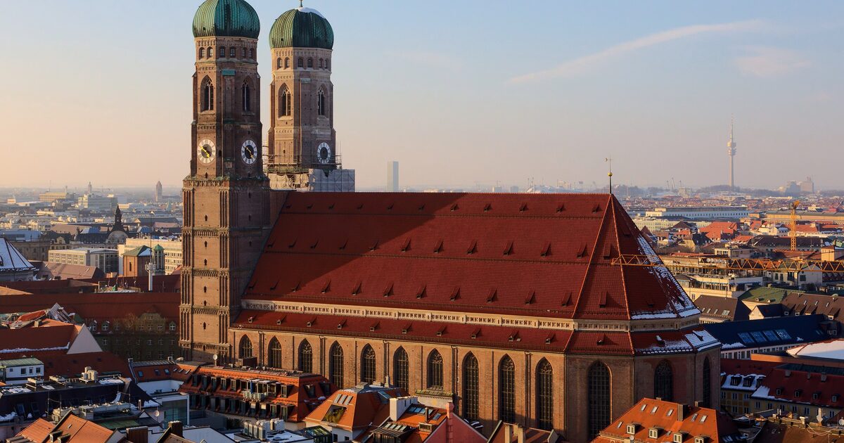 The Frauenkirche's twin domed towers and huge red roof in low evening light, with the Olympic Tower on the horizon