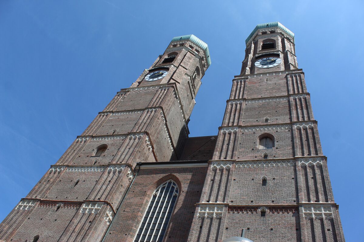 The two brick towers of the Frauenkirche seen from the street below against a clear blue sky