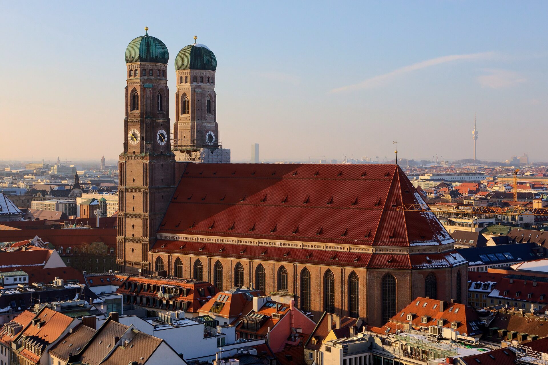 The Frauenkirche's twin domed towers and huge red roof in low evening light, with the Olympic Tower on the horizon
