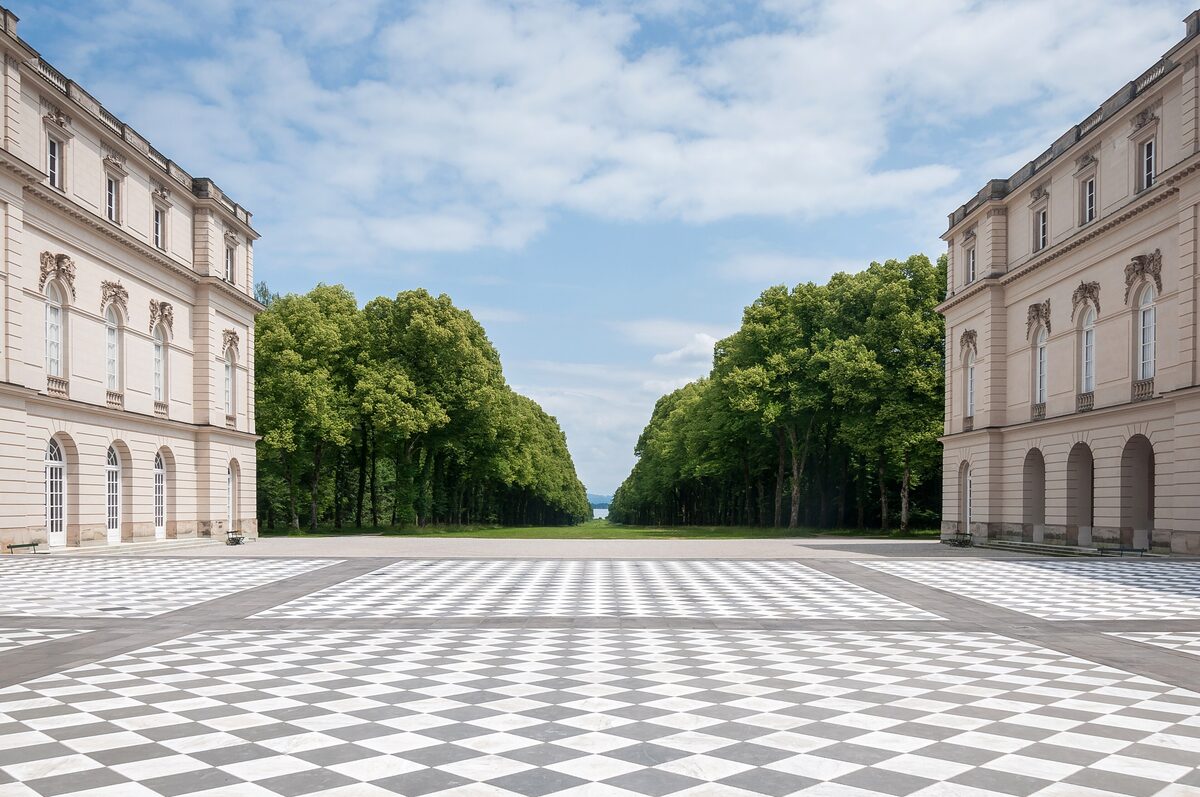 The wings of the New Palace on Herrenchiemsee around a black and white chessboard terrace, with a tree-lined avenue leading away