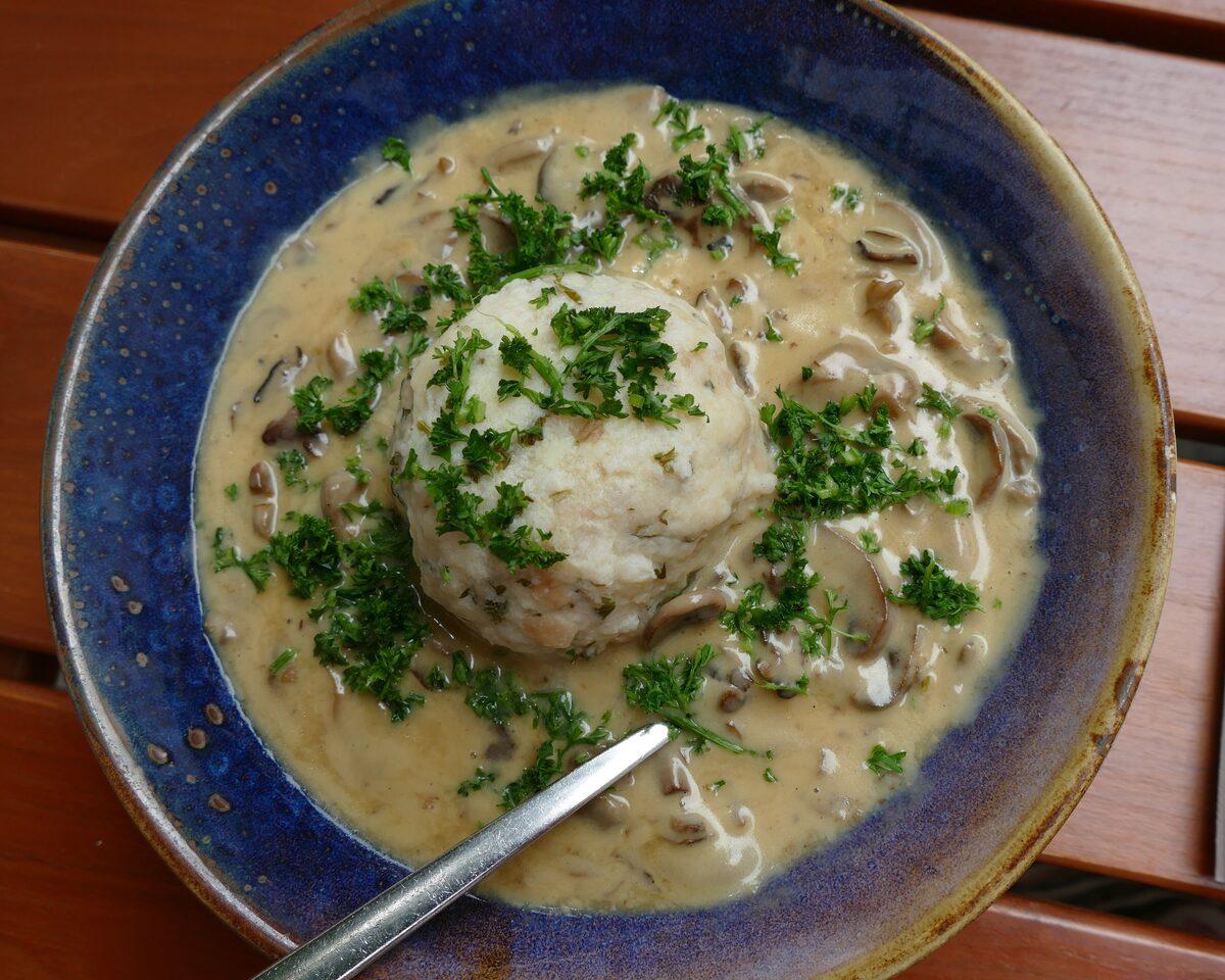 A bread dumpling in creamy mushroom sauce with chopped parsley in a blue bowl