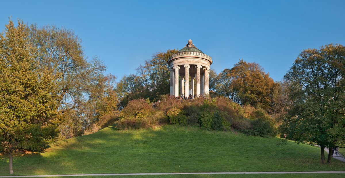 The Monopteros, a small round Greek-style temple on a grassy hill in the English Garden, with autumn trees around it
