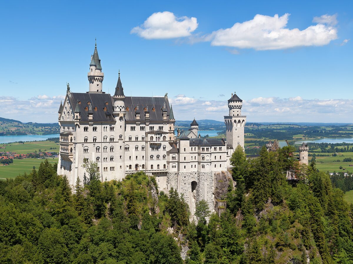 Neuschwanstein Castle on its wooded rock, with the Alpine foothills and a lake behind it