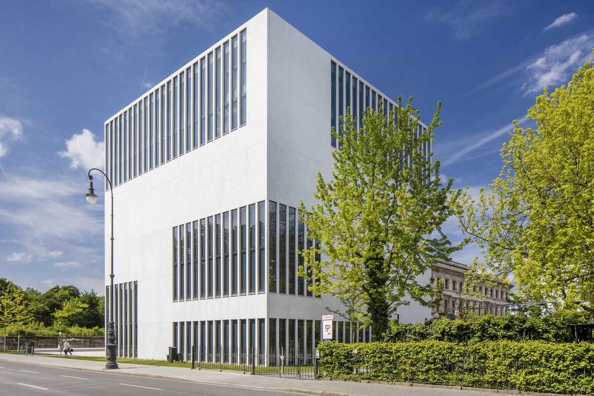 The white, cube-shaped NS-Dokumentationszentrum with its tall bands of glass, beside a leafy tree