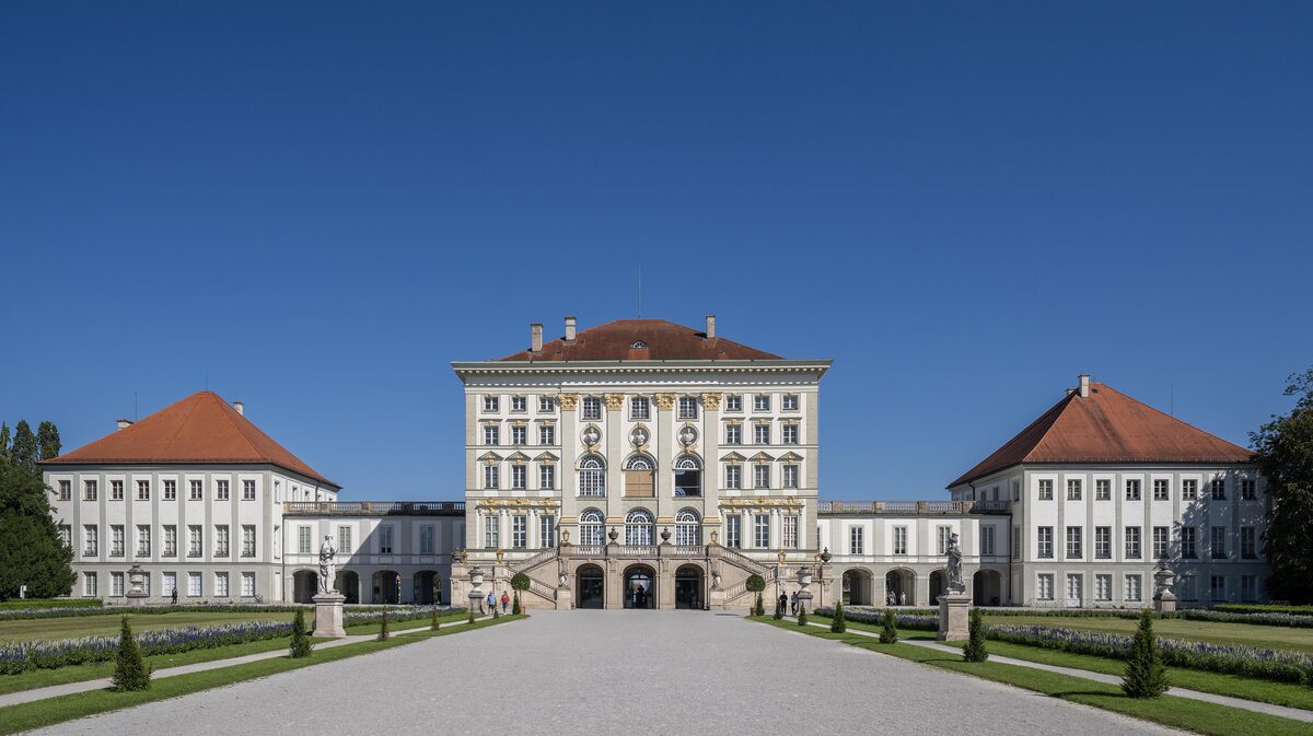 The long cream-colored front of Nymphenburg Palace and its red-roofed pavilions, seen along the garden's gravel avenue