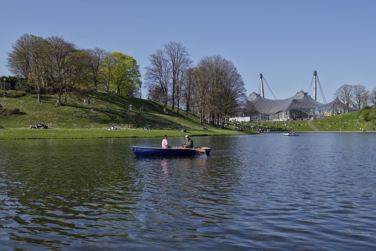 A rowing boat on the lake in the Olympiapark, with the tent roof of the stadium beyond a grassy hill