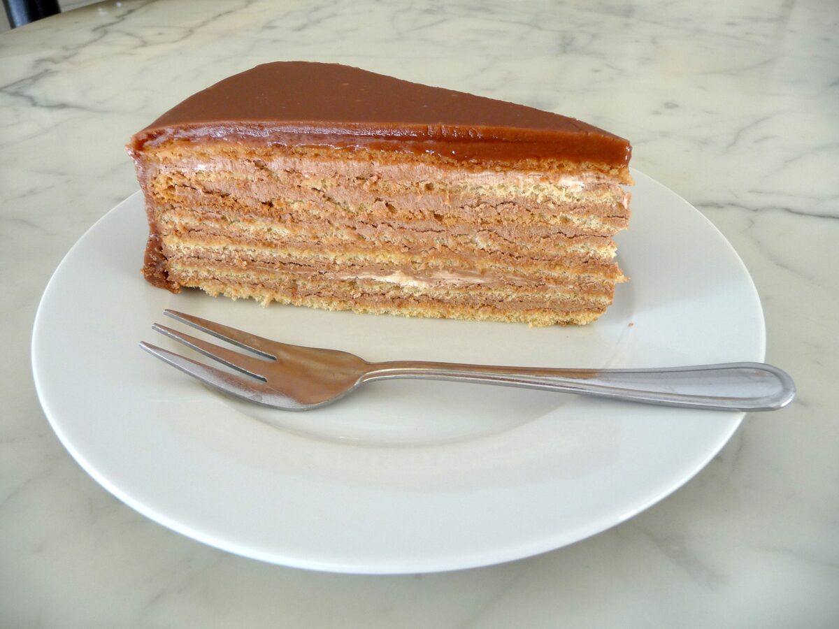 A slice of Prinzregententorte, thin sponge layers under a dark chocolate glaze, on a white plate