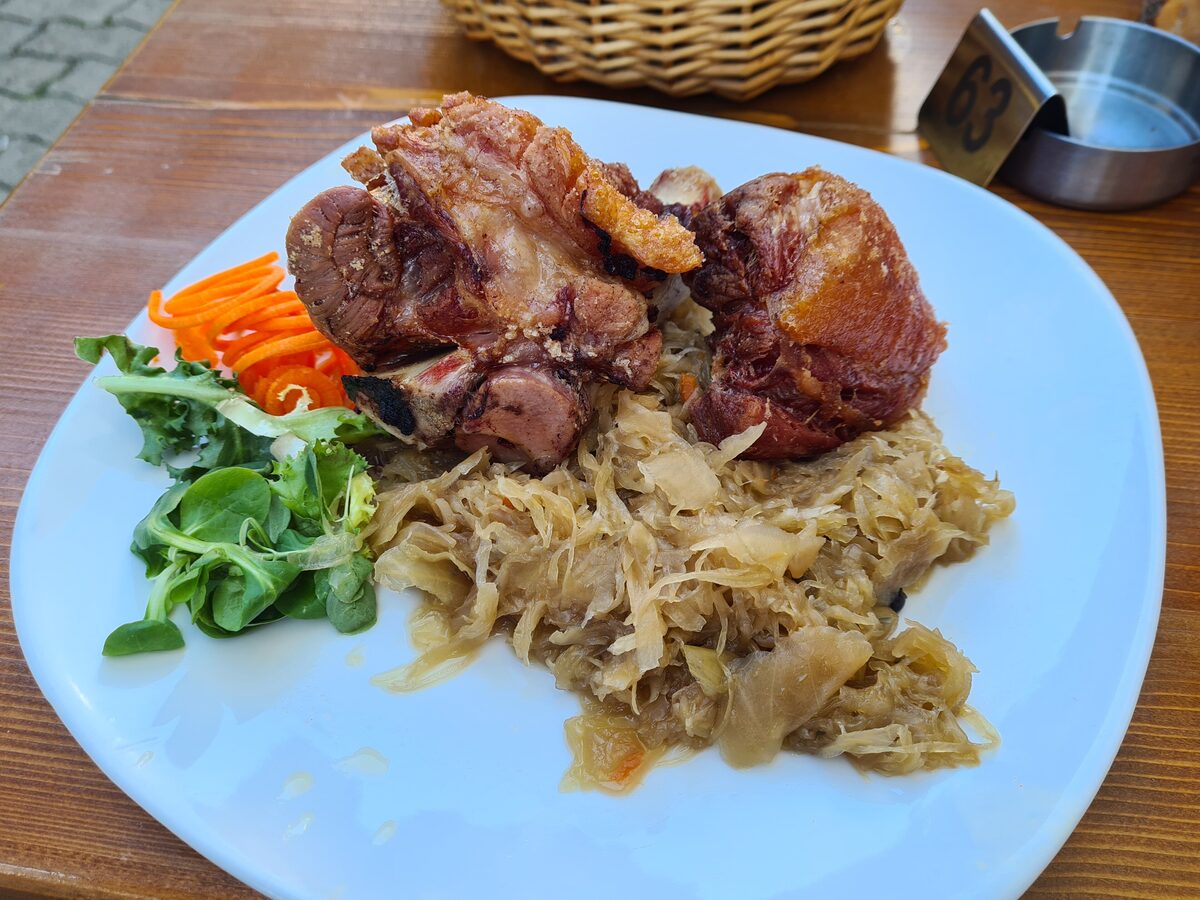 A roast pork knuckle with crisp skin, sauerkraut and a small salad on a pale blue plate