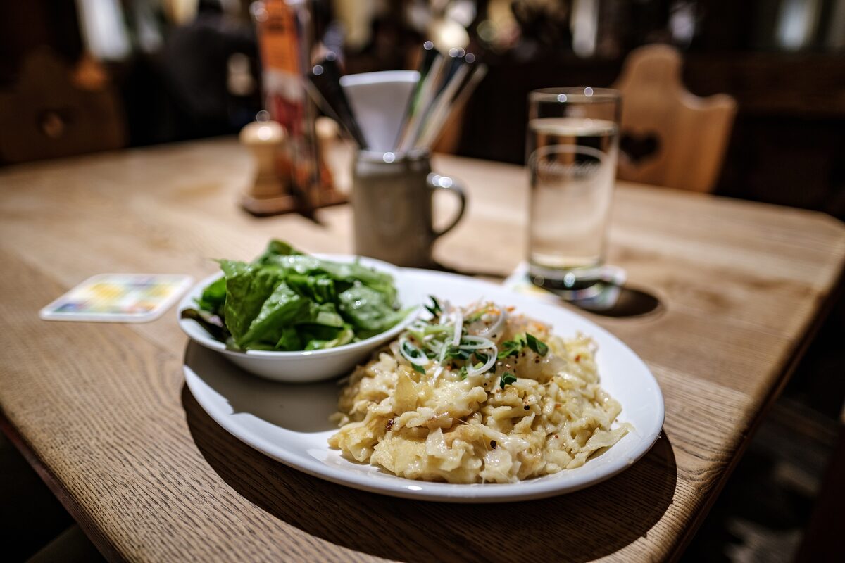 A plate of cheese Spätzle with a small green salad on a wooden table